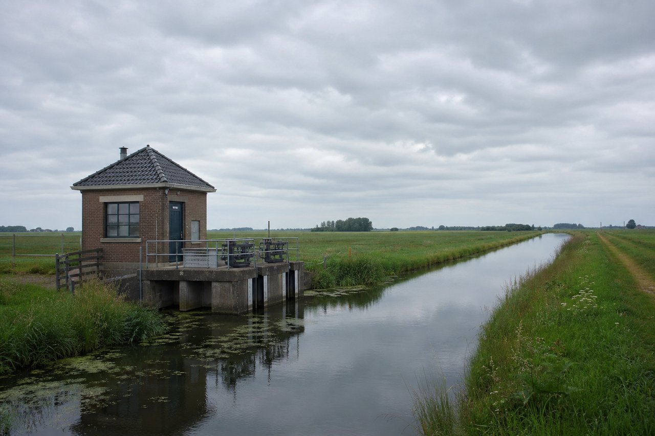 Vlak polderlandschap met een klein gemaal en een recht afwateringskanaal